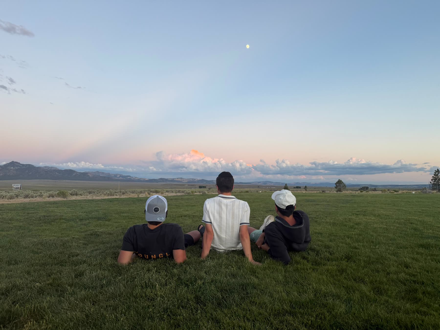 Three campers sitting in the grass watching the moon rise