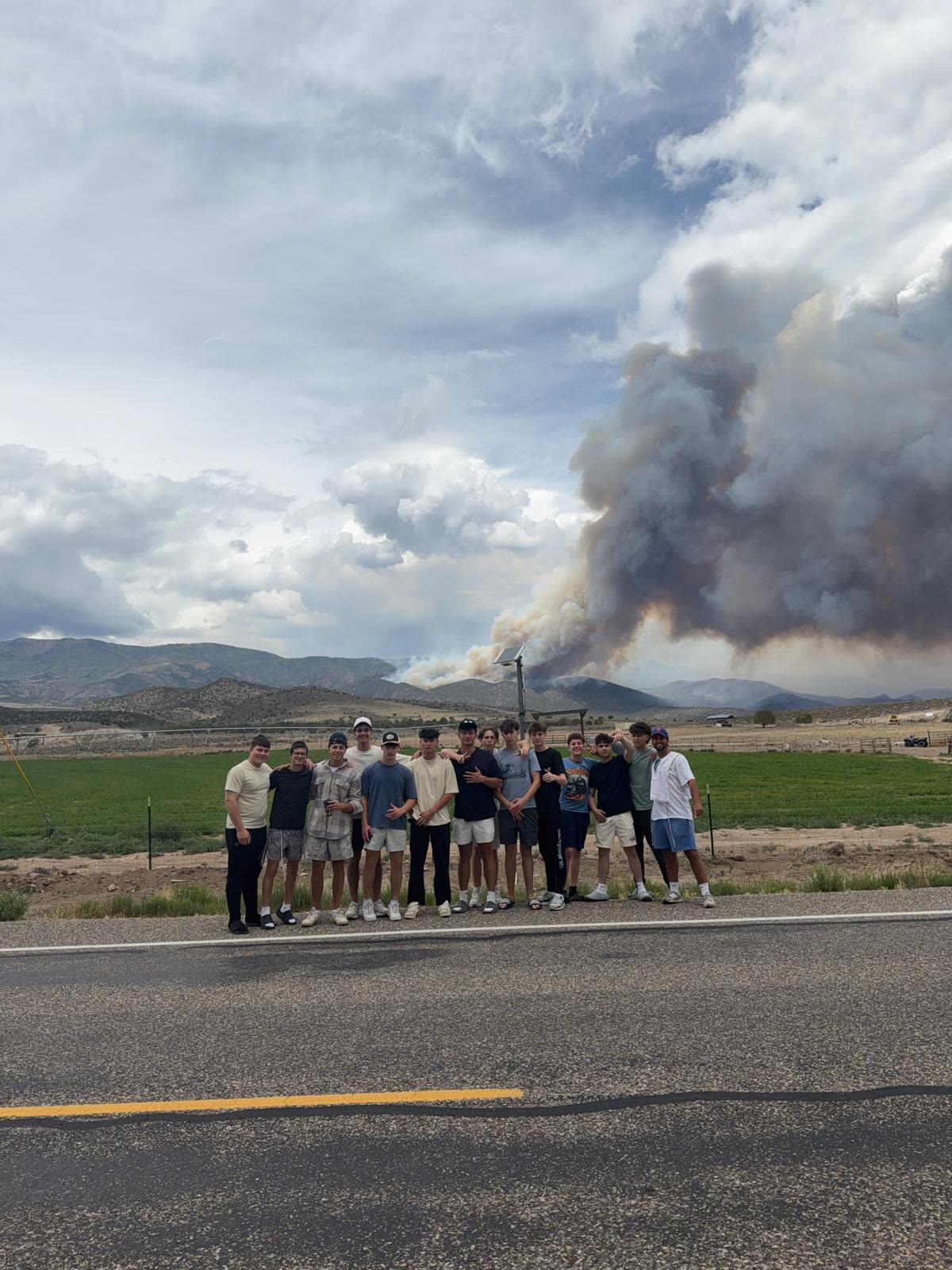Group photo on the roadside with a distant wildfire plume